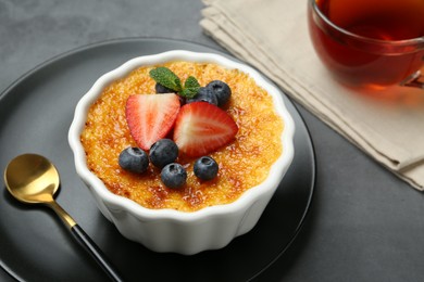 Delicious creme brulee with berries and mint in bowl on grey table, closeup