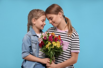 Photo of Little daughter congratulating her mom with flowers on light blue background. Happy Mother's Day
