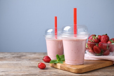 Photo of Tasty strawberry milk shake in plastic cups on wooden table