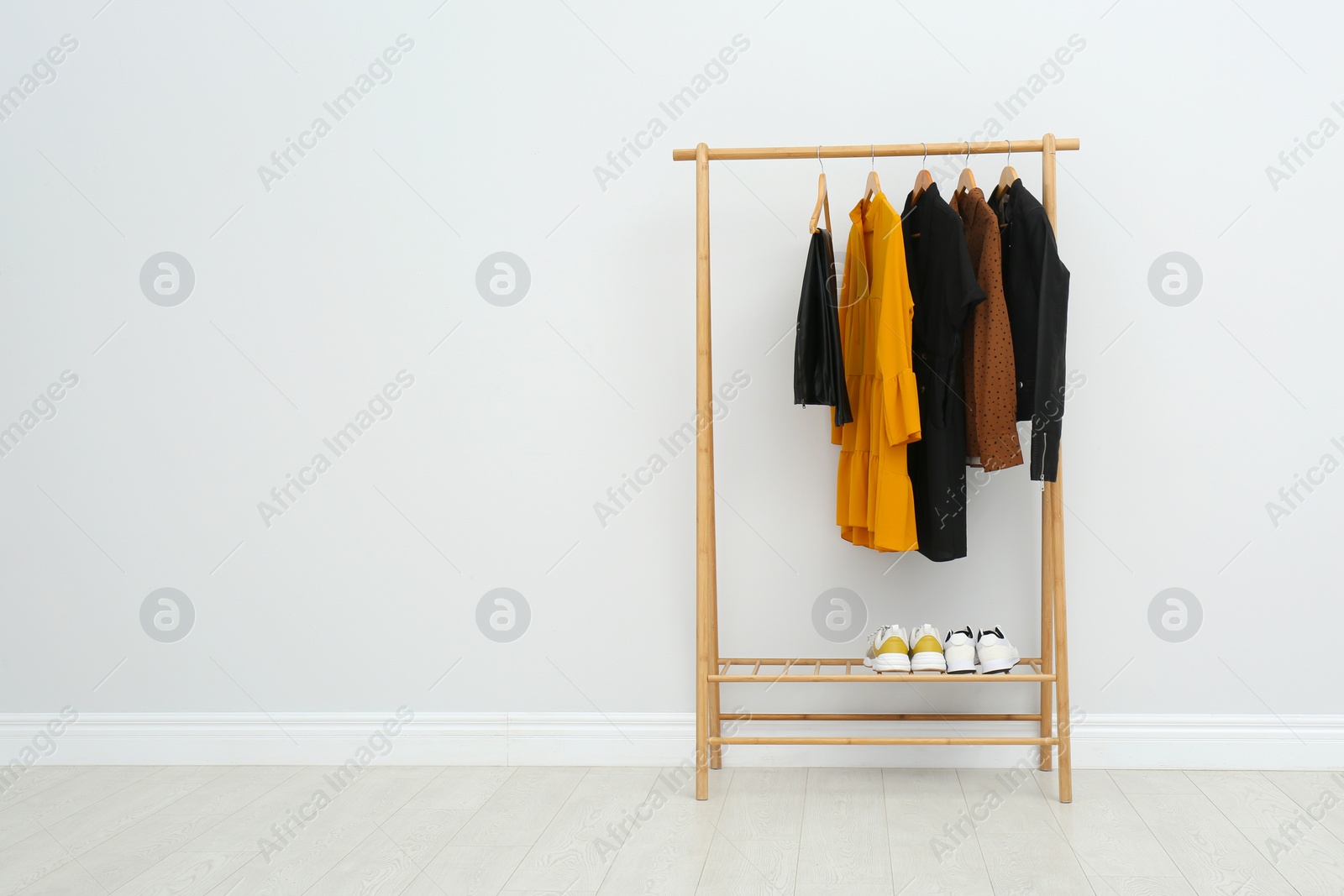 Photo of Wooden rack with stylish clothes in room. Space for text