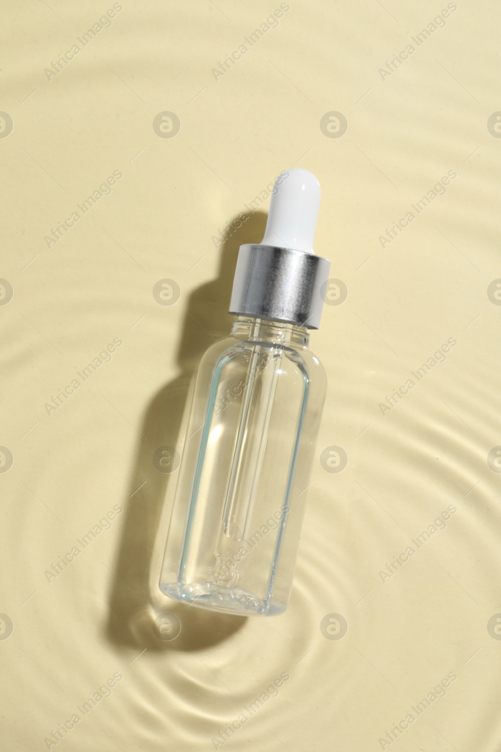 Photo of Bottle of cosmetic oil in water on beige background, top view