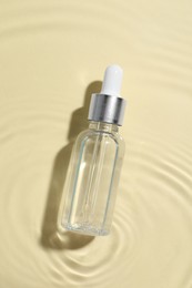 Bottle of cosmetic oil in water on beige background, top view