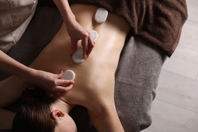 Photo of Spa therapy. Beautiful young woman lying on table during hot stone massage in salon, top view