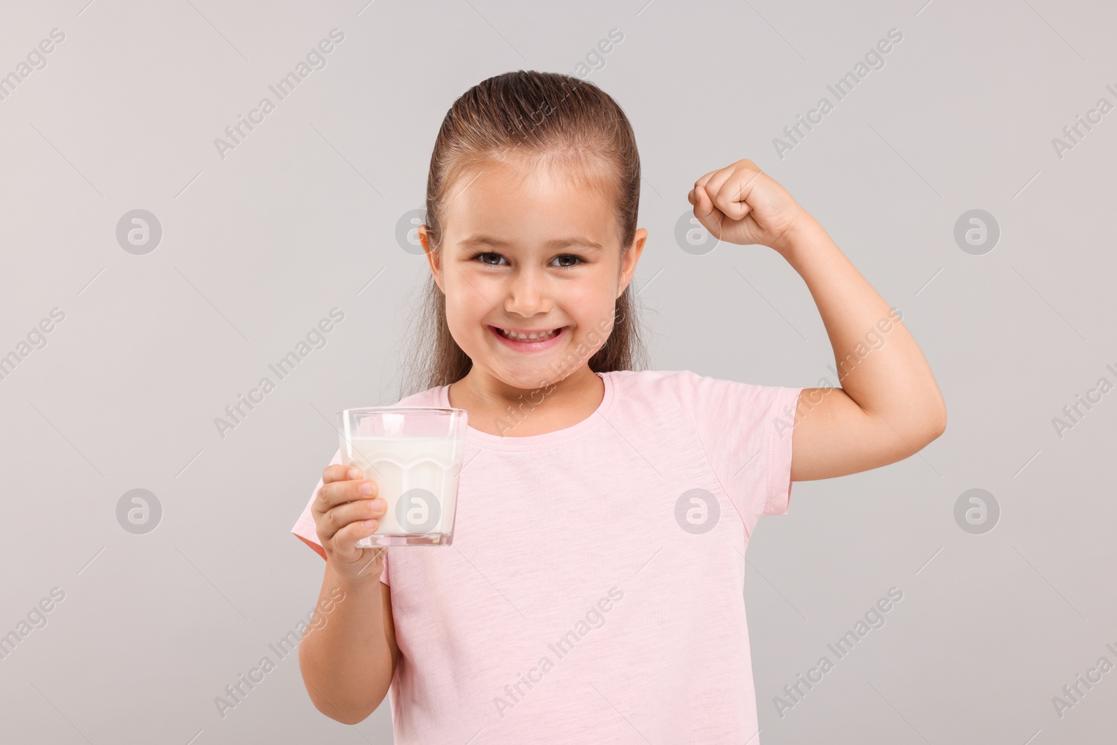 Photo of Cute girl with glass of fresh milk showing her strength on light grey background