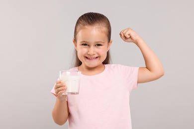 Photo of Cute girl with glassfresh milk showing her strength on light grey background