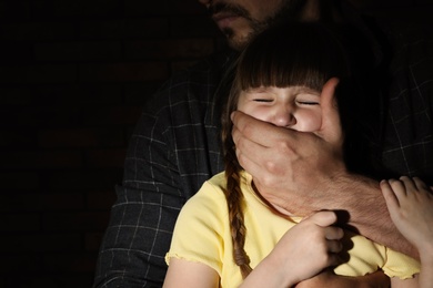 Photo of Adult man covering scared little girl's mouth on dark background, space for text. Child in danger