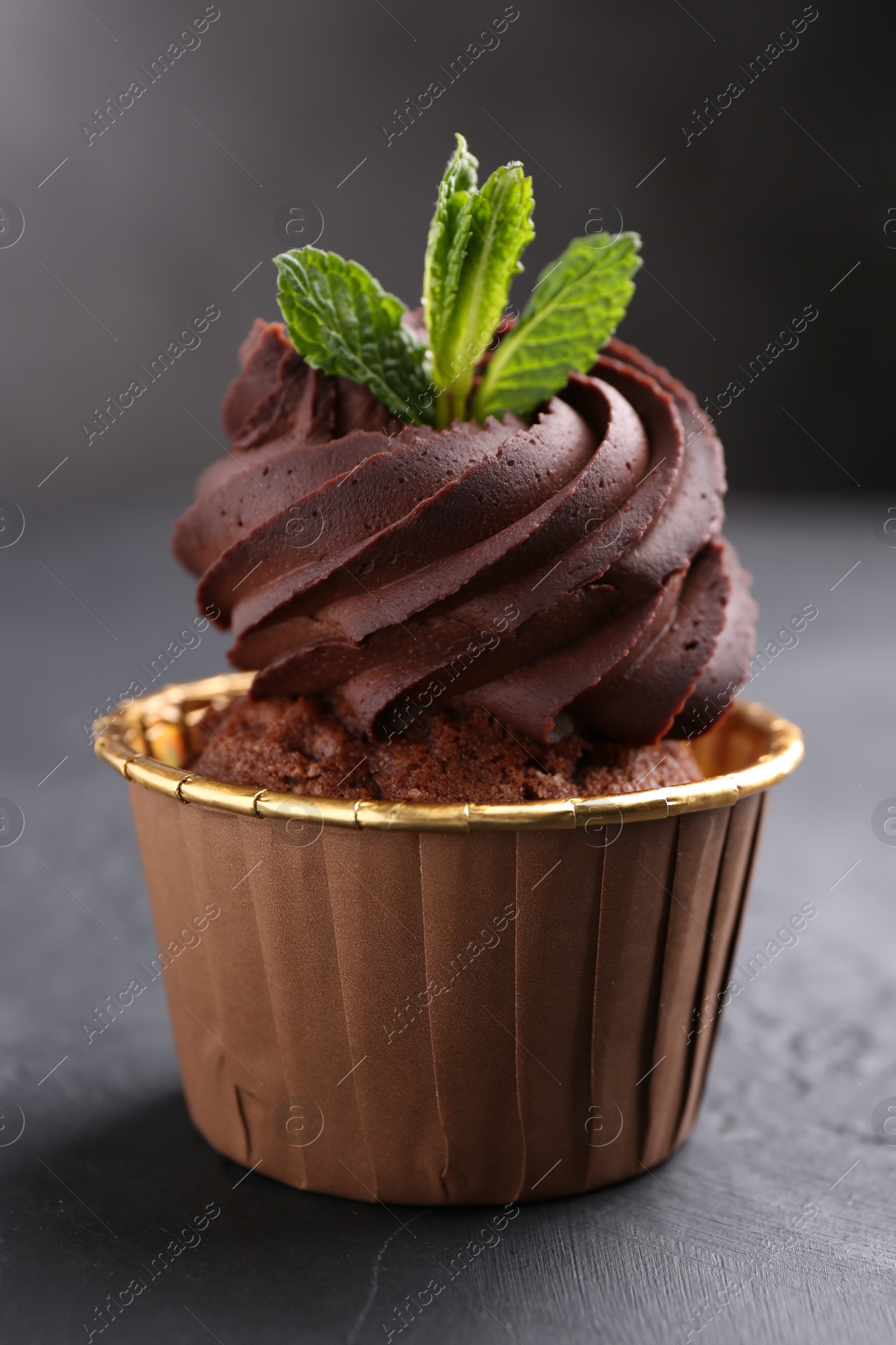 Photo of Delicious chocolate cupcake with mint on black textured table, closeup