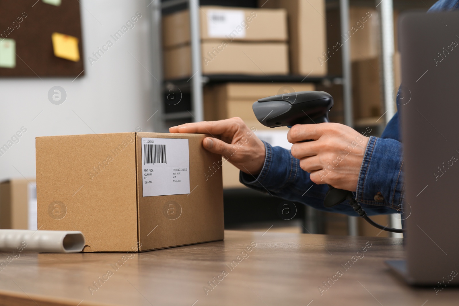 Photo of Seller with scanner reading parcel barcode at table in office, closeup. Online store