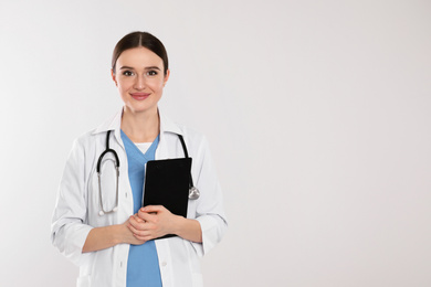 Doctor with stethoscope and clipboard on light grey background. Space for text