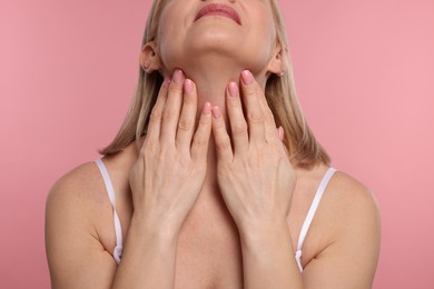 Woman touching her neck on pink background, closeup