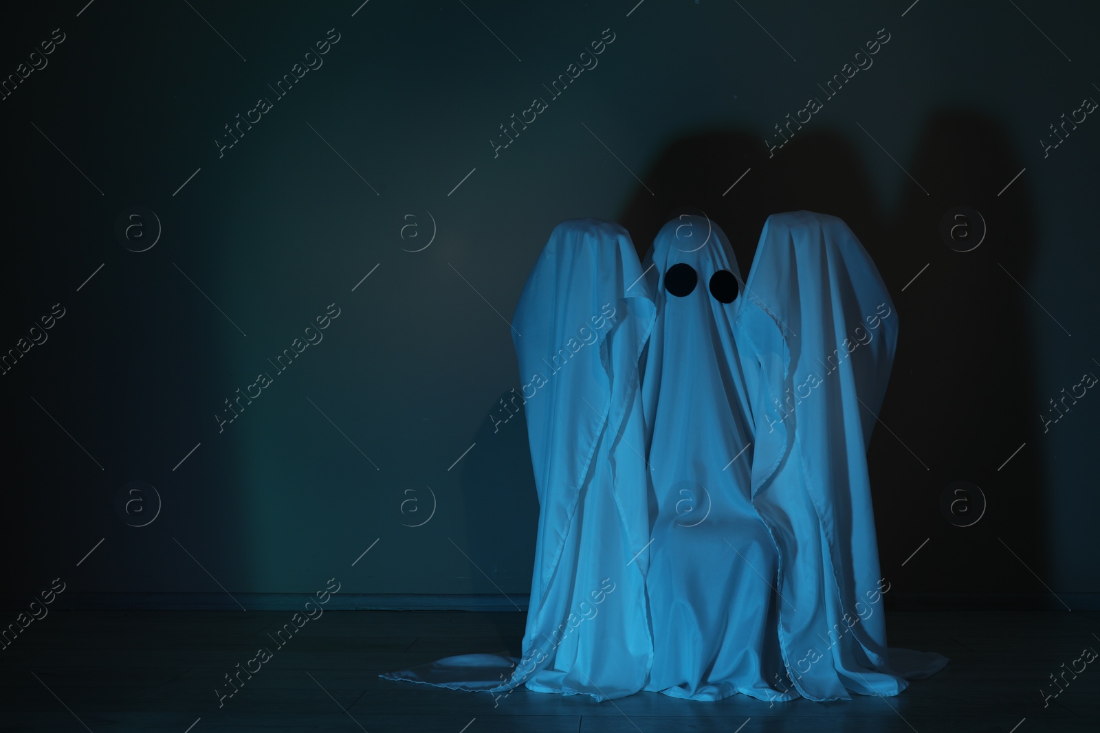 Photo of Creepy ghost. Woman covered with sheet in color light, space for text