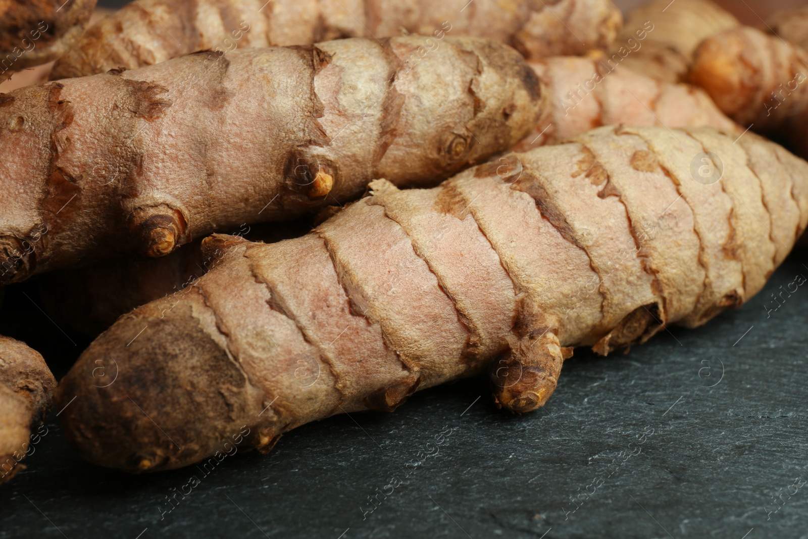 Photo of Many raw turmeric roots on black textured table, closeup