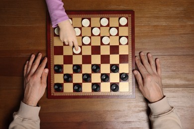 Photo of Man playing checkers with child at wooden table, top view