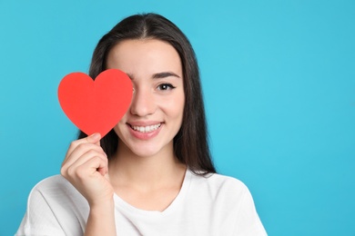Photo of Portrait of beautiful young woman with paper heart on color background, space for text