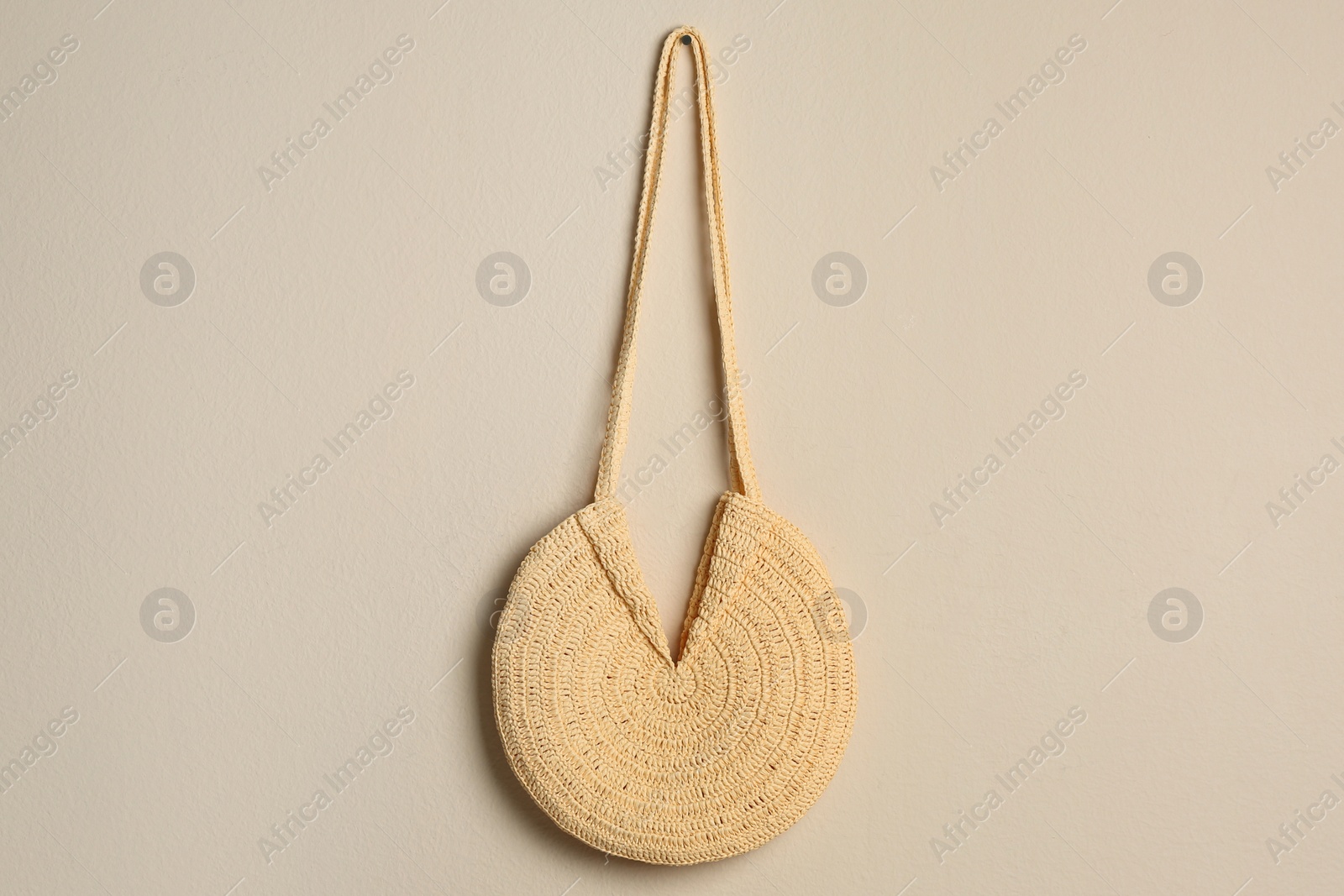 Photo of Elegant woman's straw bag hanging on beige background