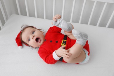 Photo of Cute baby wearing festive Christmas costume lying in crib, above view