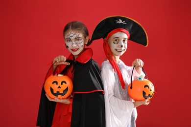 Photo of Cute little kids with pumpkin candy buckets wearing Halloween costumes on red background