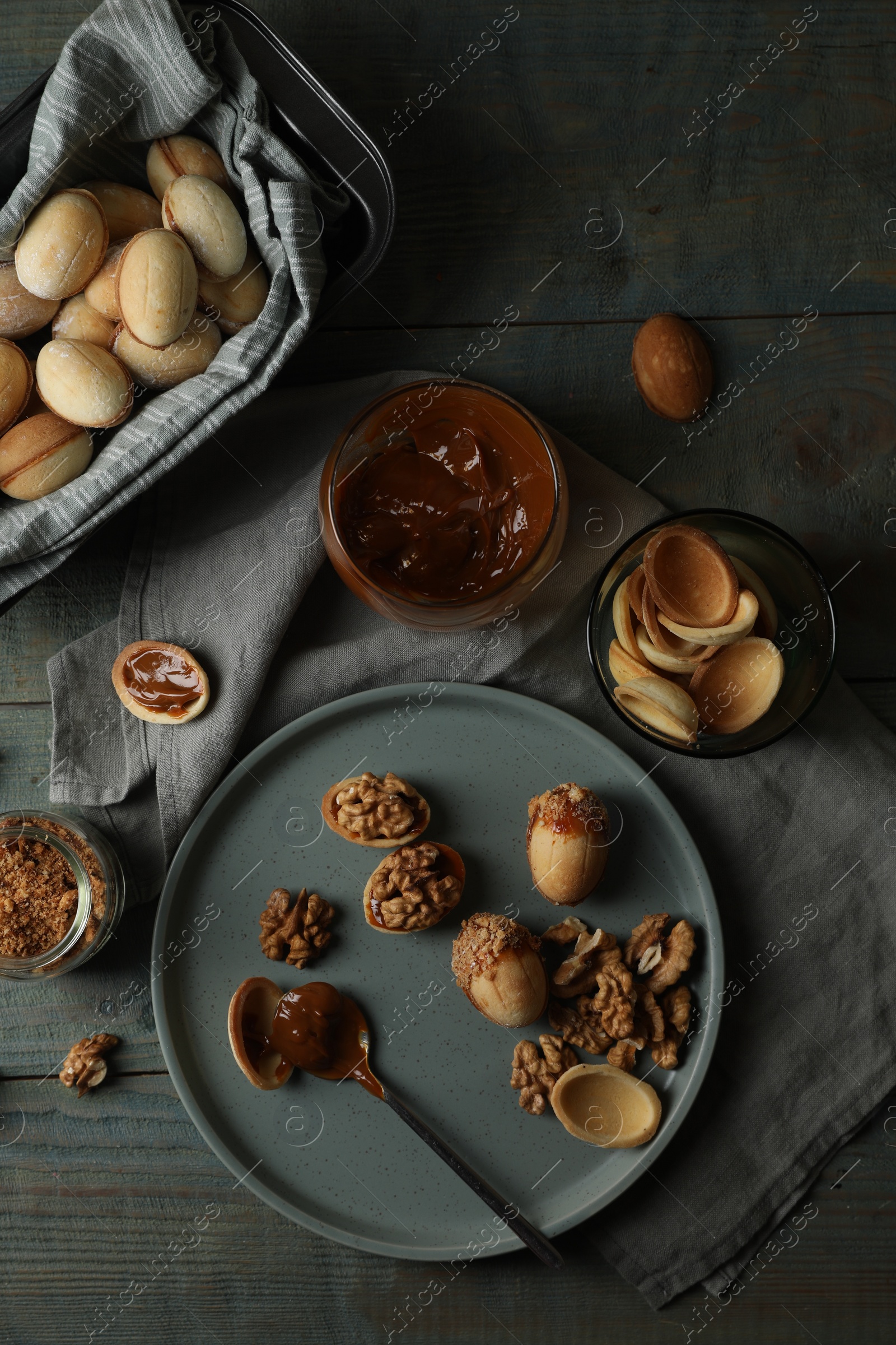 Photo of Freshly baked homemade walnut shaped cookies and boiled condensed milk on wooden table, flat lay