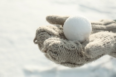 Photo of Woman in knitted mittens holding snowball outdoors, closeup