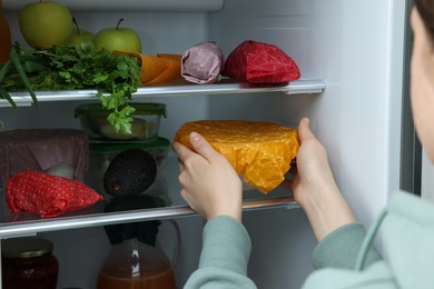 Photo of Woman taking bowl covered with beeswax food wrap from refrigerator, closeup