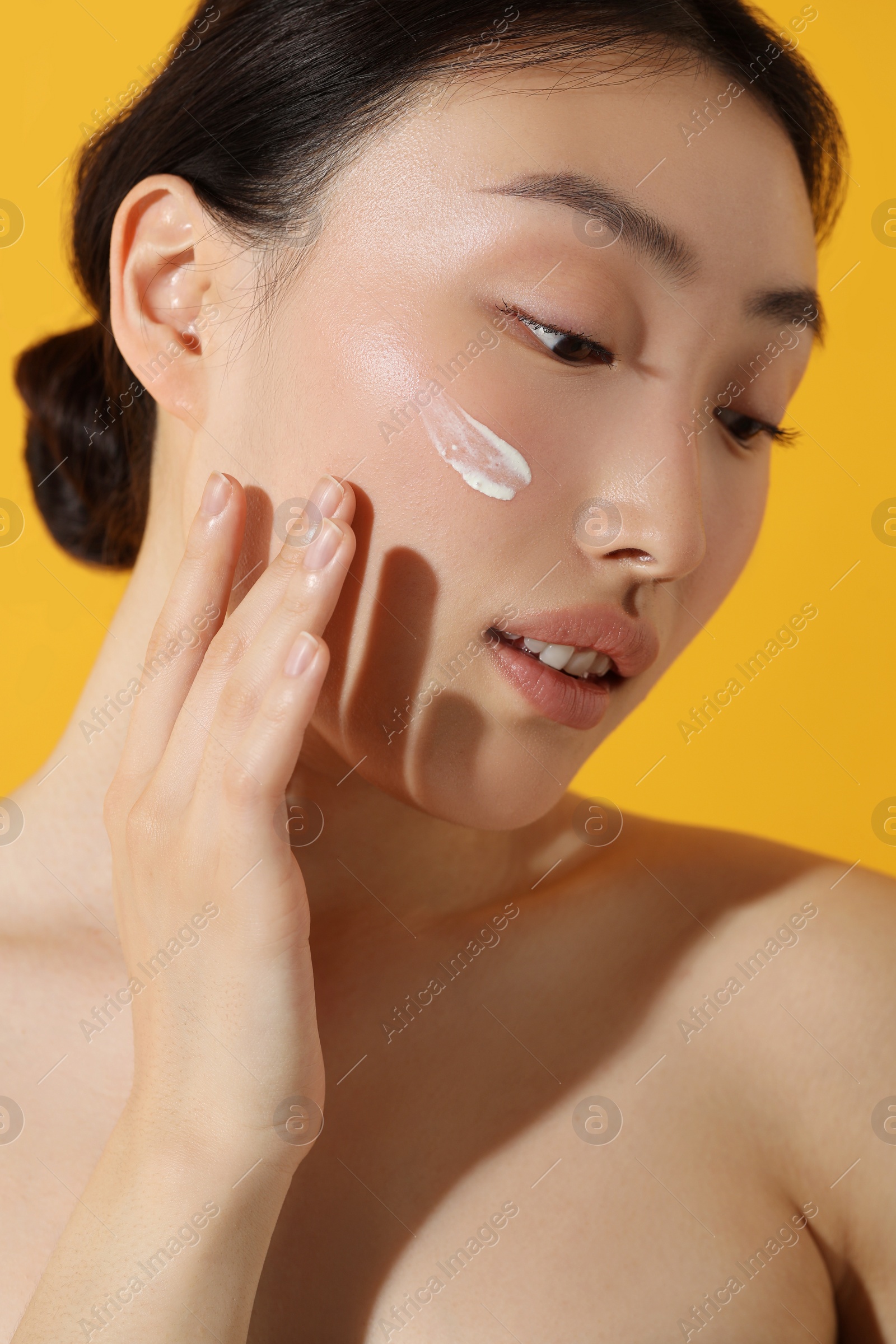 Photo of Beautiful young woman with sun protection cream on her face against orange background