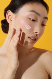 Beautiful young woman with sun protection cream on her face against orange background