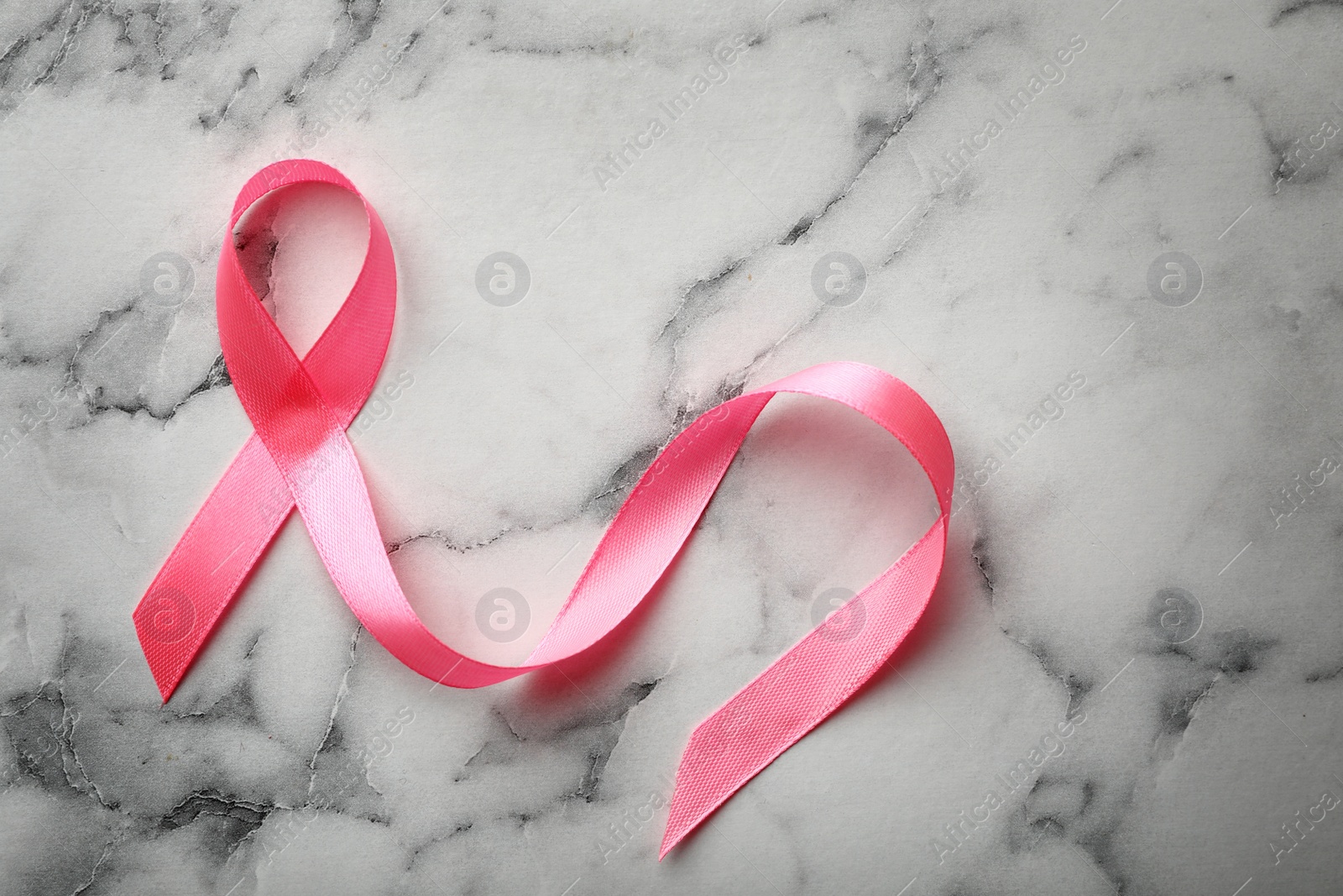 Photo of Pink ribbon on marble background, top view. Breast cancer awareness concept