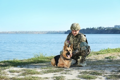 Man in military uniform with German shepherd dog near river, space for text
