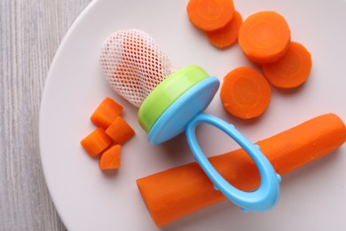 Photo of Nibbler with boiled carrot on white wooden table, top view. Baby feeder