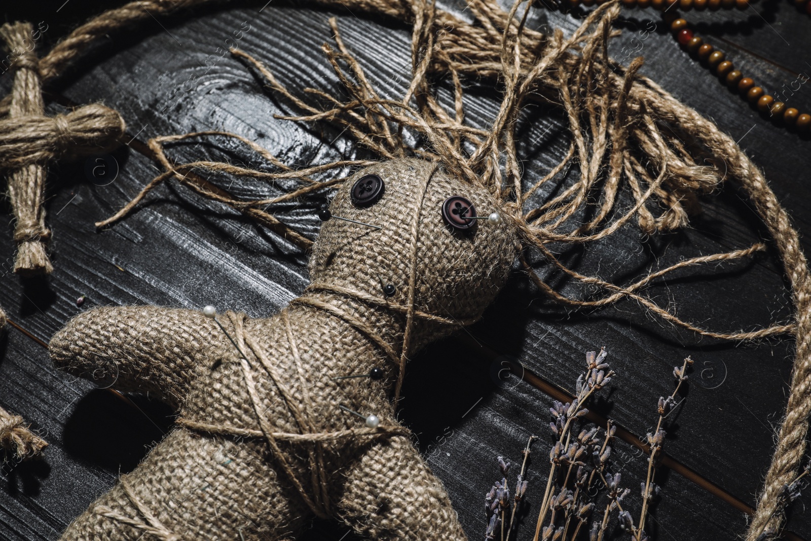 Photo of Female voodoo doll with pins surrounded by ceremonial items on black wooden background, closeup
