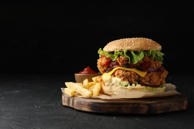 Photo of Delicious burger with crispy chicken patty, french fries and sauce on black table. Space for text