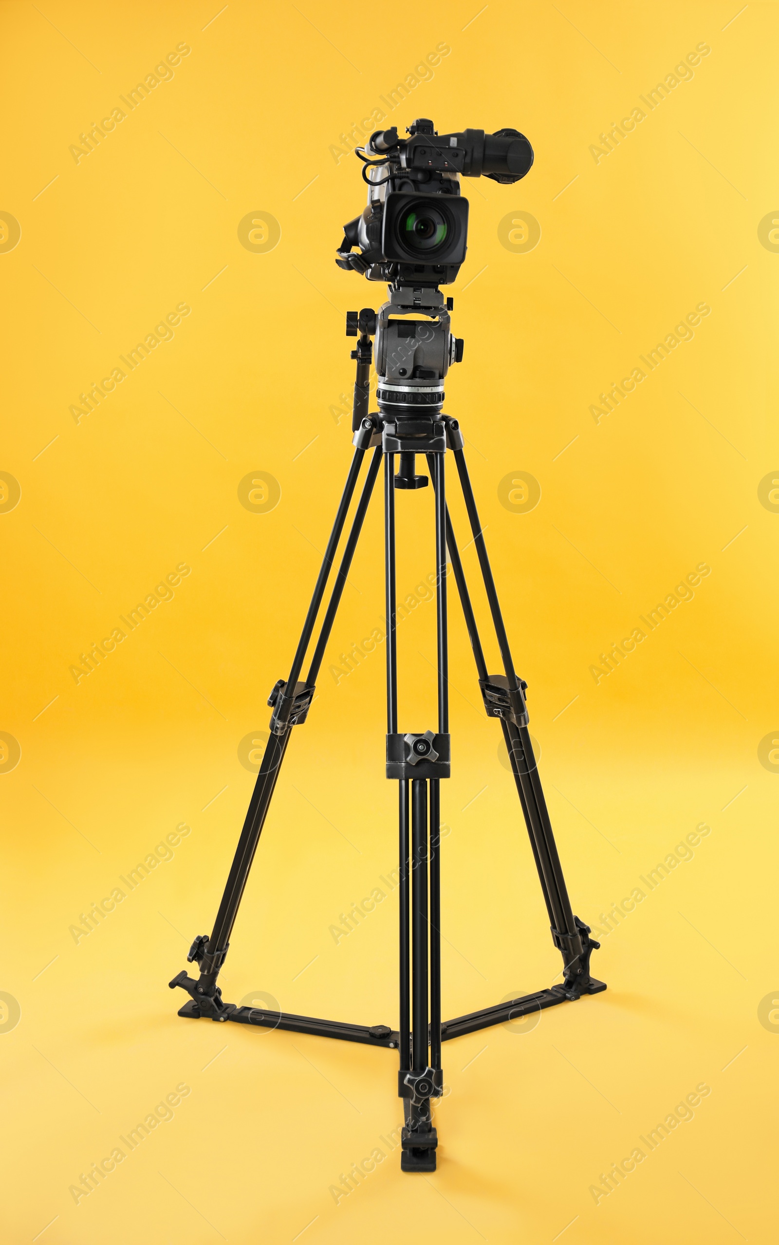 Photo of Modern professional video camera on yellow background