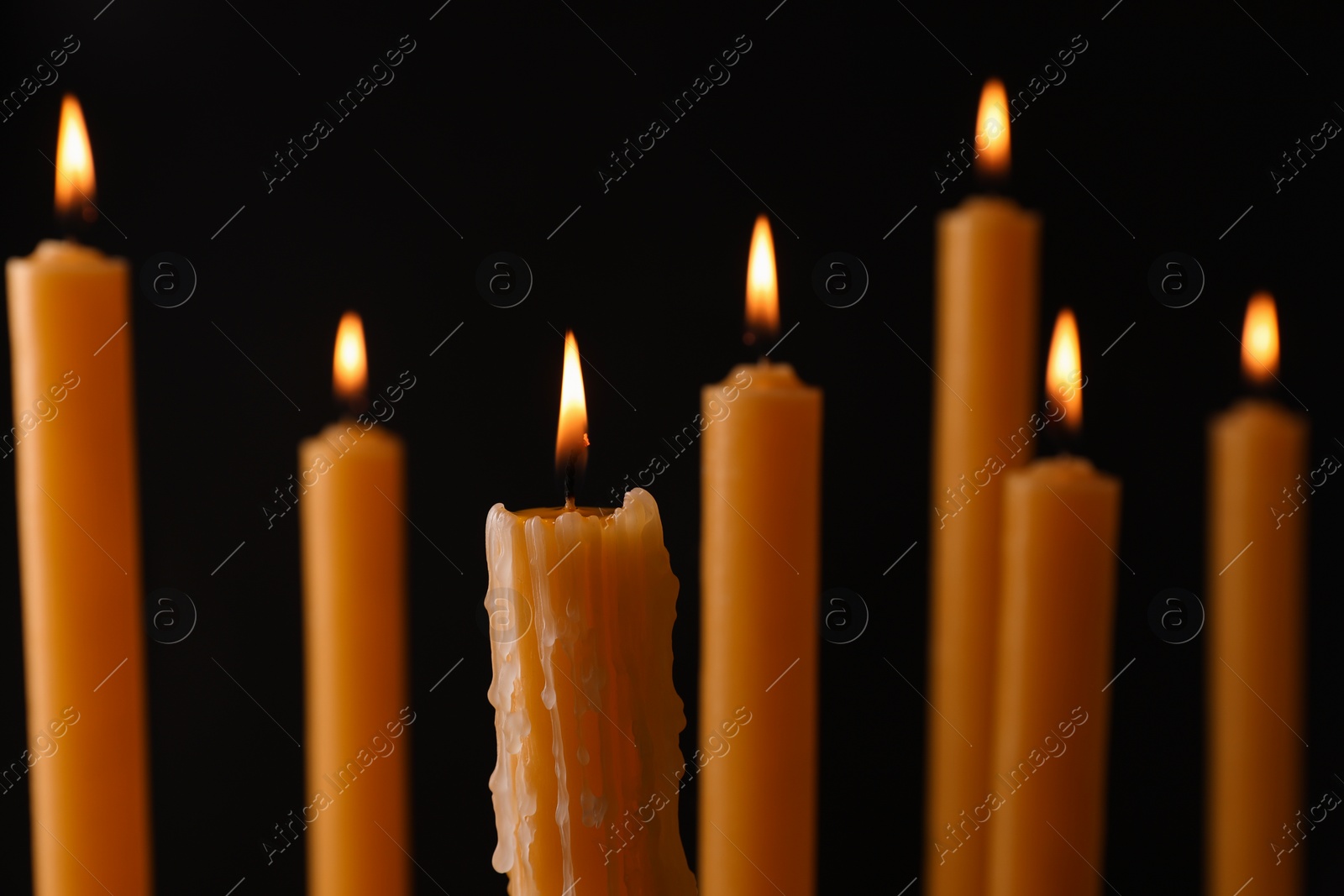 Photo of Many burning church candles on black background, closeup