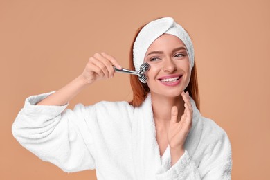 Photo of Young woman massaging her face with metal roller on pale orange background