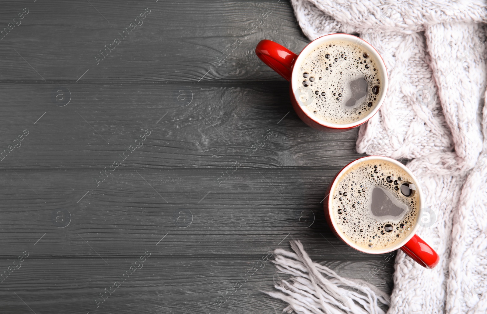 Photo of Flat lay composition cups of hot coffee and knitted scarf on grey wooden background, space for text. Winter drink