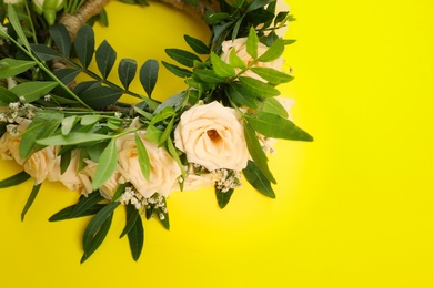 Wreath made of beautiful flowers on yellow background, space for text