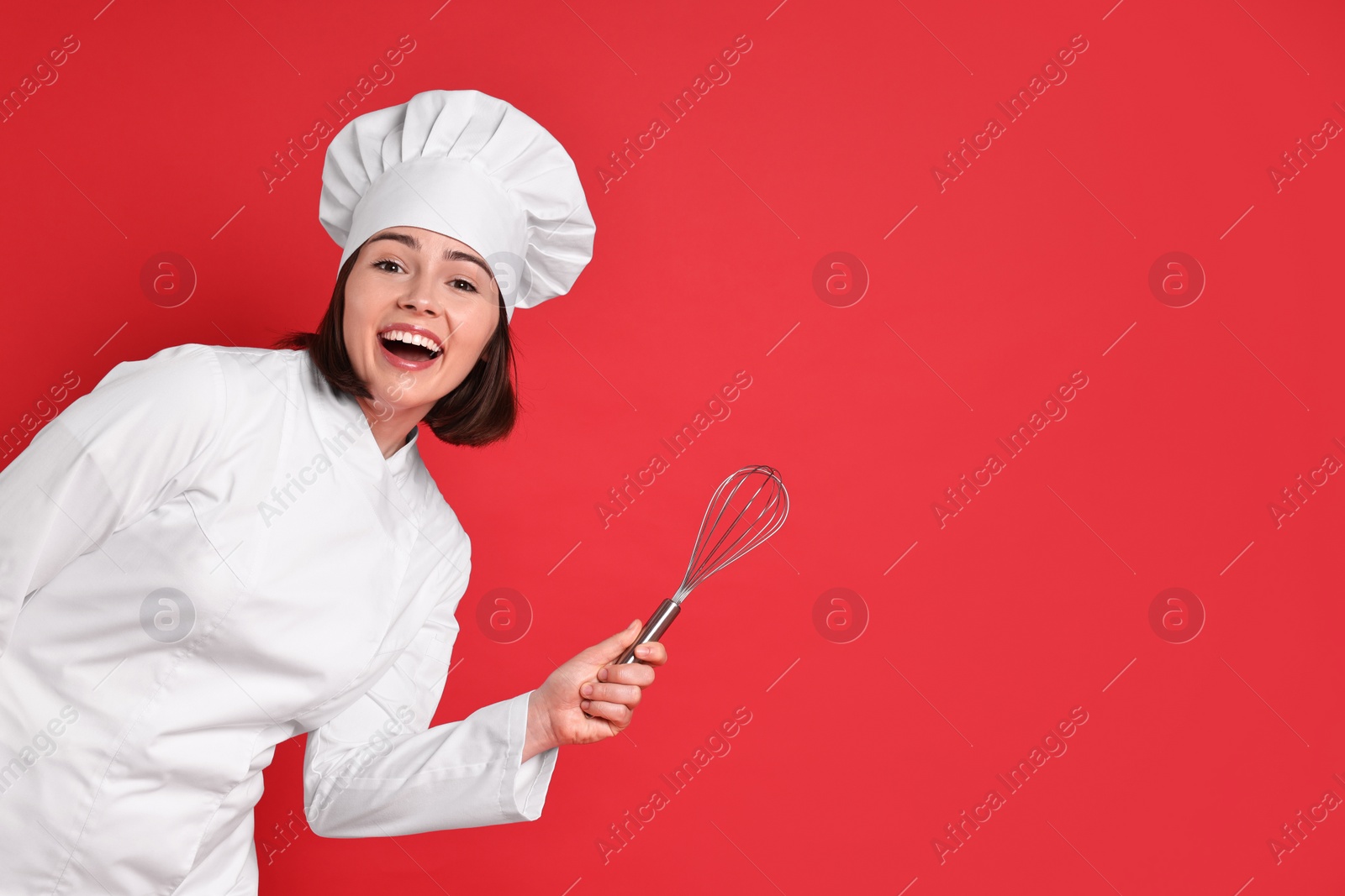 Photo of Happy confectioner holding whisk on red background, space for text