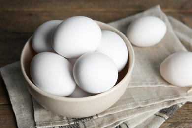 Photo of Many fresh raw chicken eggs in bowl on wooden table