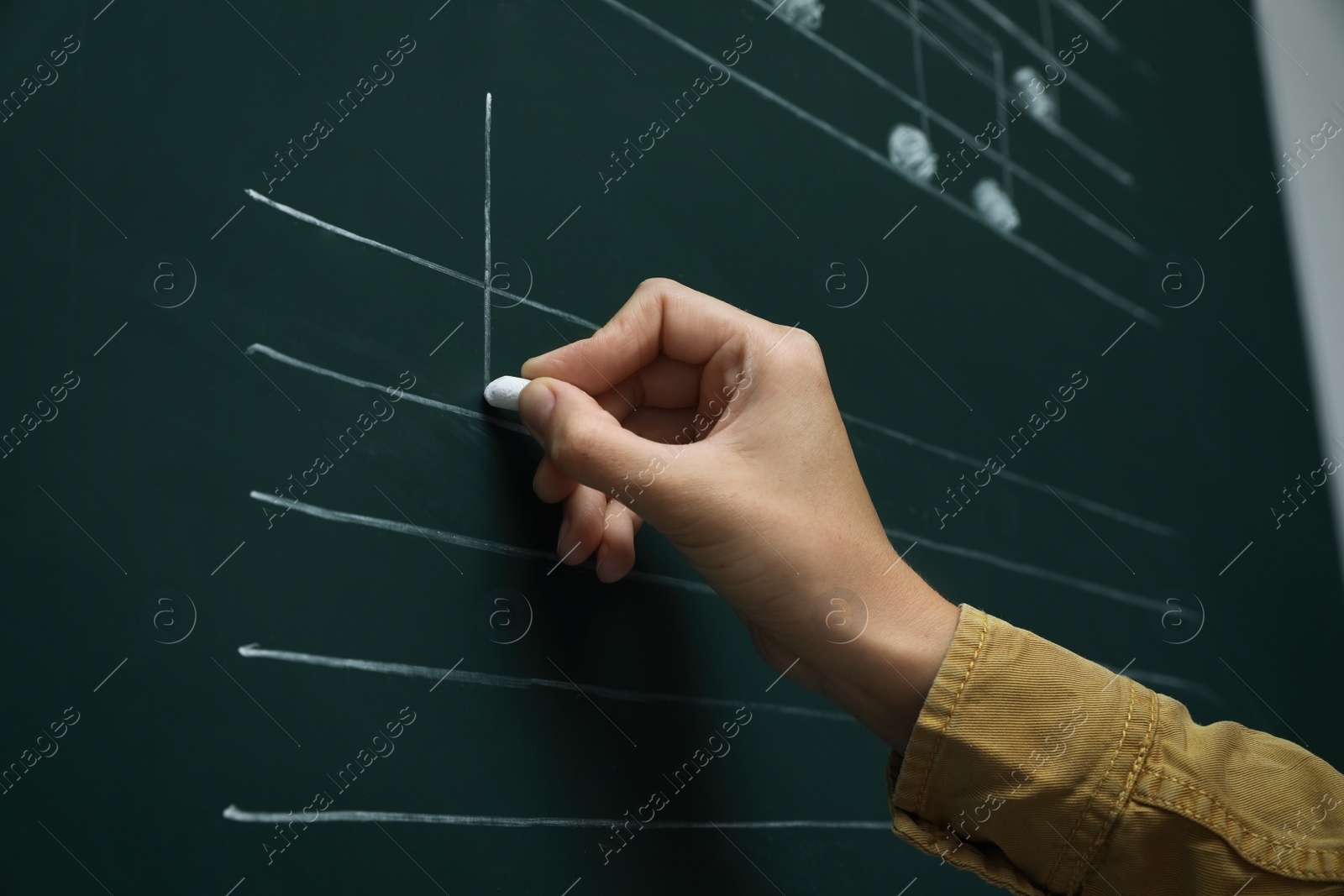 Photo of Teacher writing music notes with chalk on greenboard, closeup