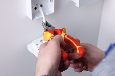 Photo of Professional repairman fixing electric house appliance with pliers indoors, closeup