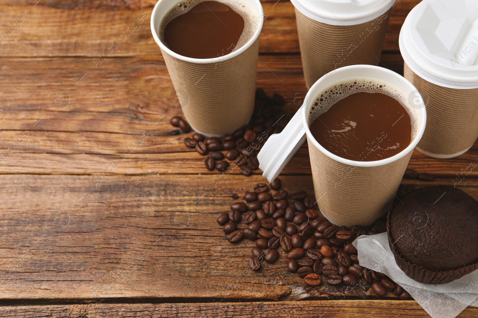 Photo of Coffee to go. Paper cups with tasty drink, muffin and beans on wooden table. Space for text