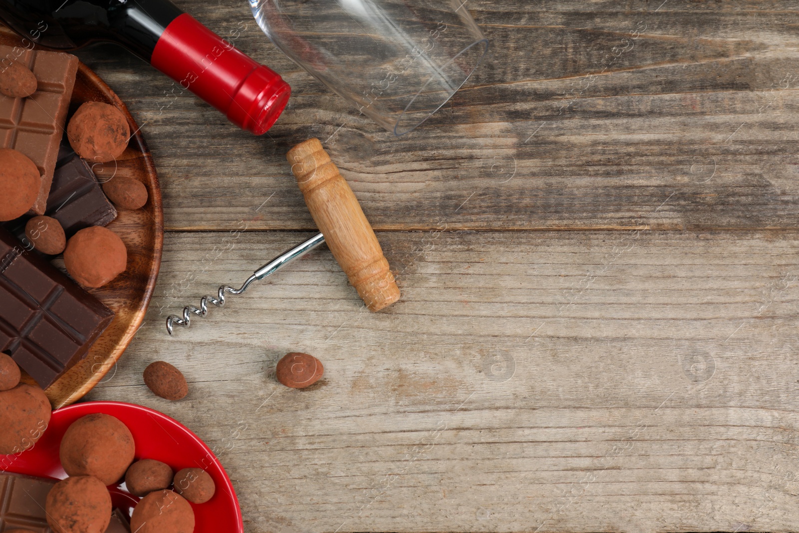 Photo of Bottle of red wine, glass, chocolate sweets and corkscrew on wooden table, flat lay. Space for text