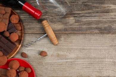 Photo of Bottle of red wine, glass, chocolate sweets and corkscrew on wooden table, flat lay. Space for text