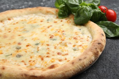 Delicious cheese pizza, basil and tomatoes on black textured table, closeup