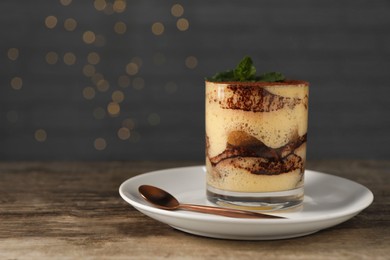 Photo of Tasty tiramisu and mint in glass on wooden table, space for text