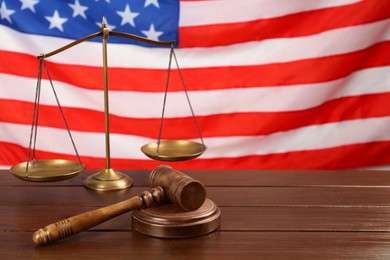 Photo of Scales of justice and gavel on wooden table against American flag. Space for text