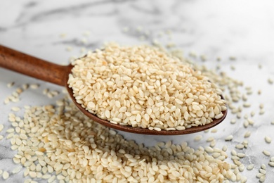 Spoon with sesame seeds on white marble table, closeup