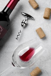 Corkscrew with wine bottle, glass and stoppers on light grey stone table, flat lay