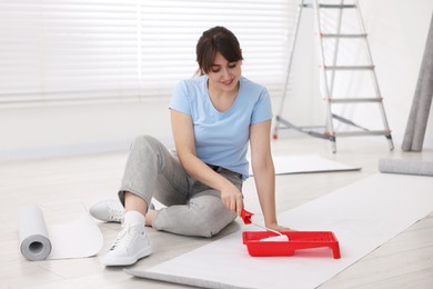 Woman applying glue onto wallpaper sheet in room