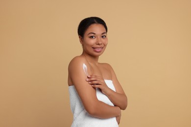 Photo of Young woman applying body cream onto shoulder on beige background